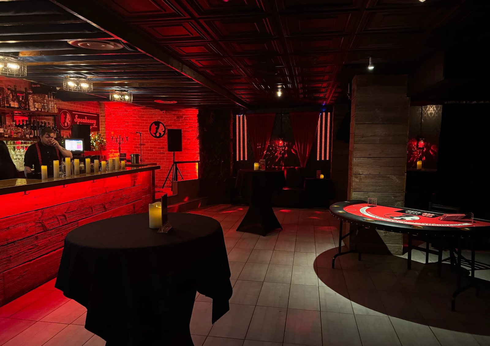The lounge under red light, set with cocktail tables, a blackjack table and the bar staffed